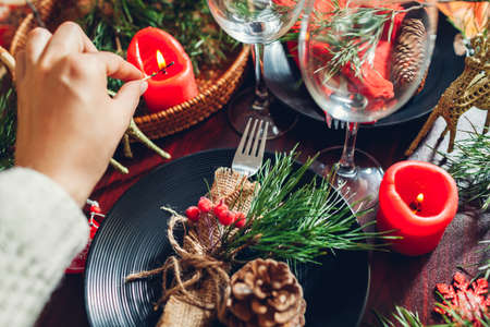Festive Christmas dinner table setting for two decorated with fir branches, red candles, cones,...