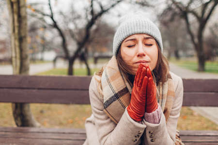 Sad devastated young woman sitting on bench in autumn park crying and praying. Mental health and religion. Fall depressionの写真素材