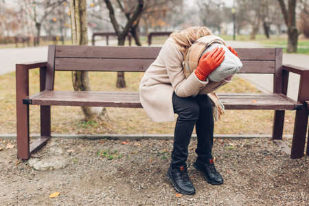 Depression and loneliness. Upset devastated young woman sitting on bench in autumn park crying covering face with hands. Mental healthの写真素材