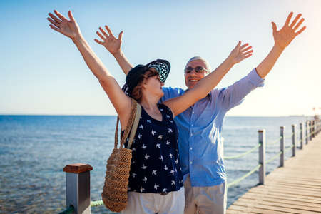 Senior family couple raising arms on pier by Red sea. Happy retired people celebrating vacation in Sharm el Sheikh in Egypt.の写真素材