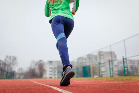 Young woman athlete running on sportsground in autumn. Close up of sneakers and female legs. Active healthy lifestyleの写真素材