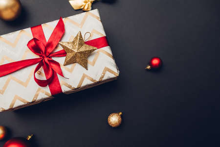 Christmas and New year present wrapped in holiday paper and decorated with red ribbon and ornaments on black background.の写真素材