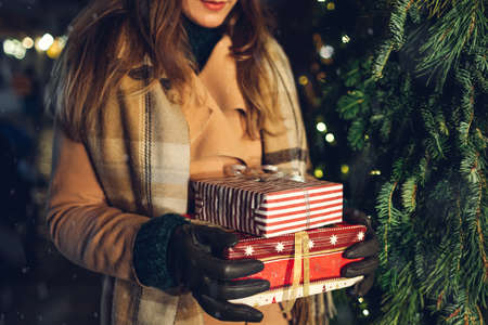 Close up of Christmas gift boxes in female hands. Woman holding presents by New year outdoor decor