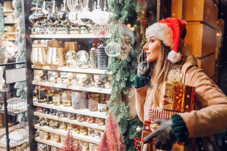 Happy woman in Santas hat holding presents gift boxes by store showcase on city street at Christmas season.の写真素材