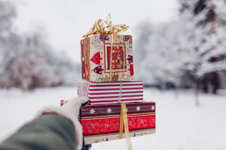Close up of heap of red Christmas presents gift boxes in snowy winter park outdoors in female hand. Festive New year holiday seasonの写真素材