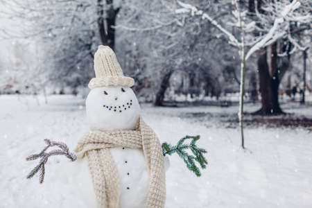Happy snowman made outdoors in snowy winter park dressed in knitted white hat, scarf with fir branches in hands. Seasonal fun activitiesの写真素材