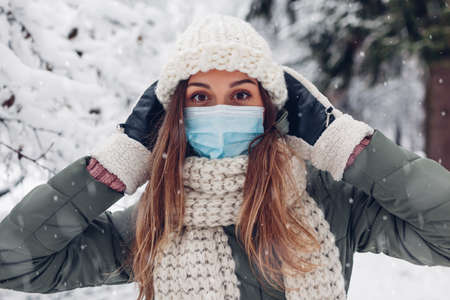 Young womanwearing medical protective mask in snowy winter park outdoors. Covid-19 coronavirus pandemic safety measuresの写真素材