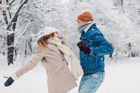 Young man and woman jumping and tossing snow up in winter park. Couple having fun playing outdoorsの写真素材