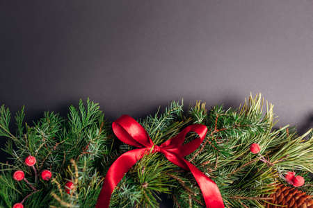 Christmas and New Year garland made of fir, pine evergreen branches, rose hips, cones decorated with red ribbon bow on black background. Festive decorの写真素材