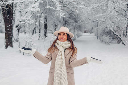 Happy fashionable young woman playing with snow tossing it in cold winter park wearing stylish warm clothes and having fun outdoors. Seasonal activitiesの写真素材