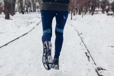 Young woman athlete running in snowy winter park. Close up of sneakers and legs. Active healthy lifestyleの写真素材