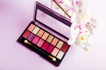 Palette of new colourful eyeshadows, pigments, glitter with orchid flowers. Make-up products on purple backgroundの写真素材