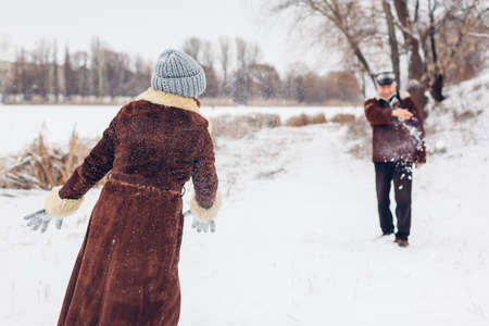 Senior family couple playing snowballs outdoors during snowy winter weather. Elderly people having...