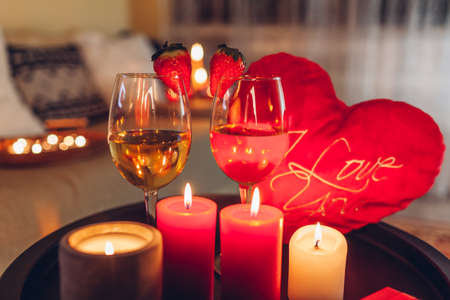 Valentines day celebration at home with champagne wine glasses with strawberries on top surrounded with candles by heart shaped pillow. Setting for twoの写真素材