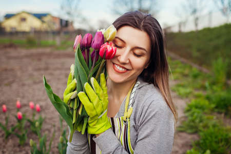 Gardener picked bouquet of fresh tulips in spring garden. Young happy woman smiling holding flowers. Close up portraitの写真素材