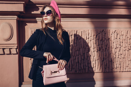 Female beauty, fashion. Stylish woman wearing pink beret, glasses holding purse on city street outdoors. Spring clothes, accessories.の写真素材