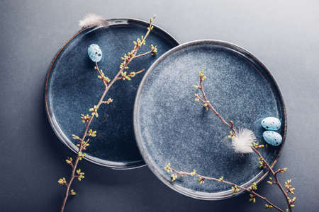 Easter decor. Handmade dish decorated with blue eggs, feathers and spring branches. Ceramic plate on...