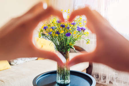 Woman showing heart with fingers around blue and yellow flowers. No war in Ukraine. Independence day symbol of Ukraineの写真素材