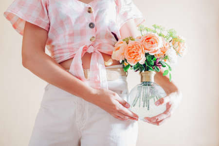 Young woman holding vase with bouquet of fresh flowers. Floral arrangement with orange english roses...
