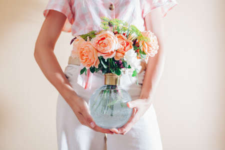 Close up of summer bouquet of flowers in transparent glass vase. Woman florist holds arrangement with orange roses. Interior decorの写真素材