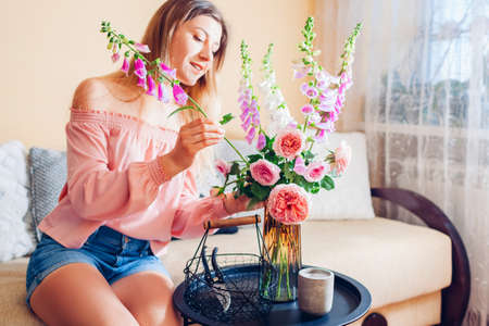 Woman makes bouquet of roses and foxgloves flowers picked in basket in vase at home. Interior and summer decor.の写真素材
