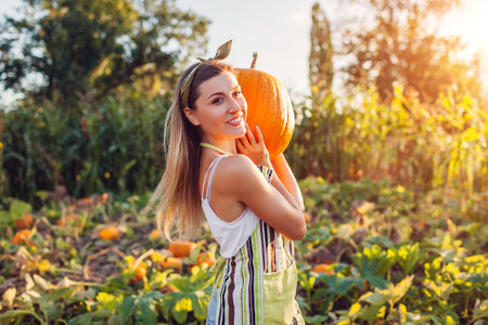 Pumpkin harvest. Portrait of young woman farmer picking autumn crop of vegetables on farm. Worker holds big pumpkinの写真素材