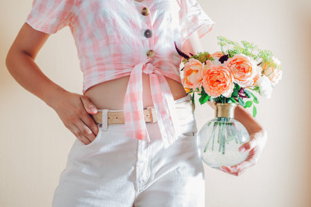 CLose up of vase with bouquet of fresh flowers in female hands. Fresh floral arrangement with orange white roses and greenery. Summer bloomsの写真素材