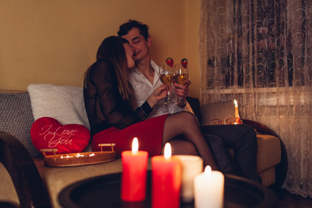 Young Valentines Day couple in love clinking glasses drinking wine with strawberries having romantic dinner with candles celebrating at home at nightの写真素材