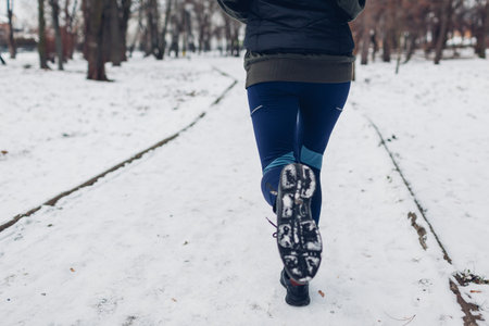 Sportive young woman athlete running in snowy winter park. Close up of sneakers and legs. Active healthy lifestyle. Outdoor workoutの写真素材