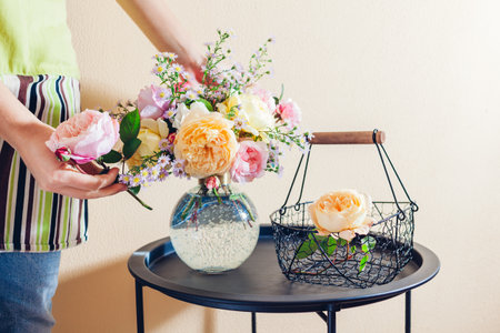 Close up of fresh english roses. Woman makes bouquet in transparent vase of orange yellow pink flowers on table at home.の写真素材