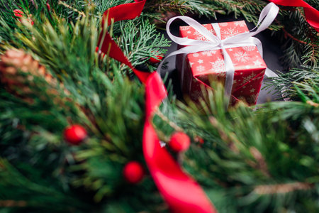 Christmas and New Year red gift box wrapped in festive paper and ribbon by inside fir wreath with ribbon. Present for winter holidays on black background. Top viewの写真素材
