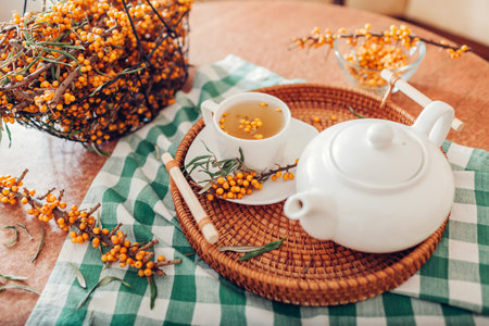 Tea with sea buckthorn berries served in cup and kettle on tray. Healthy hot drink for cold fall and winter days. Yellow fruit on harvested branchesの写真素材