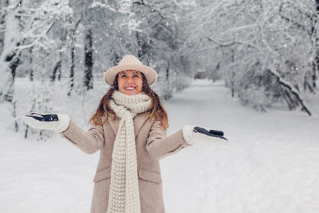 Happy fashionable young woman tossing snow up in frosty winter park wearing stylish warm clothes and having fun outdoors. Seasonal activities. Spaceの写真素材
