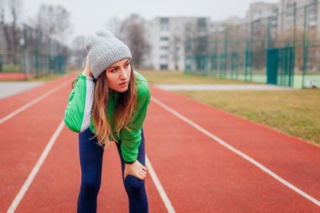 Tired exhausted runner having rest after training on winter sportsground on track. Woman working out outdoors. Sportive lifestyleの写真素材