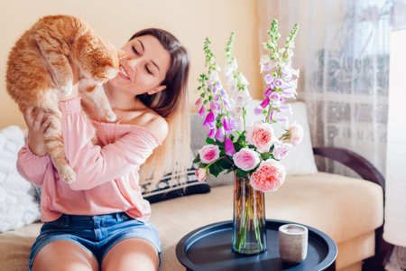 Playing with ginger cat at home. Young woman relaxing on couch in living room and holding pet.の写真素材