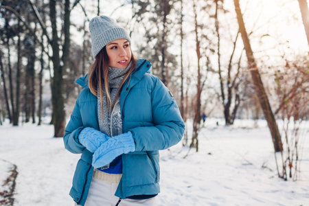 Young woman walking in snowy winter park wearing blue coat. Girl enjoys landscape wearing hat and mittens outdoorsの写真素材