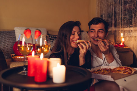 Valentines Day couple in love eating pizza drinking wine with strawberries having romantic dinner celebrating at home at nightの写真素材