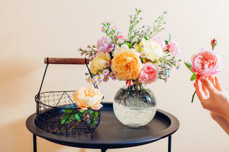 Close up of fresh english roses. Woman makes bouquet in transparent vase with orange yellow pink flowers on table at home. Interior decorの写真素材