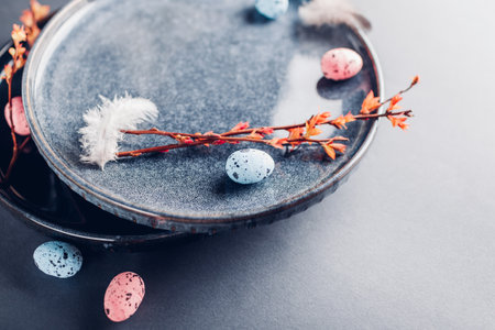Easter pottery decoration. Close up of dishes with eggs, feathers and red spring branches. Lacquered ceramic plates on grey background. Holiday setting. Spaceの写真素材