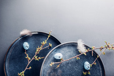 Rustic Easter dishes decorated with blue eggs, feathers and spring branches. Ceramic plate on grey background. Space. Holiday mockup. Top view of vintage potteryの写真素材