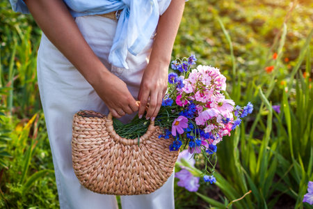 Close up of stylish straw handbag filled with blooming flowers. Woman holding summer purse with fresh bouquet. Boho rustic style. Female fashionの写真素材
