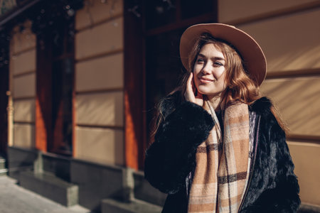 Female fashion. Stylish woman wearing black fur coat, beige hat and scarf. Spring accessories. Portrait of happy young girl on street outdoorsの写真素材