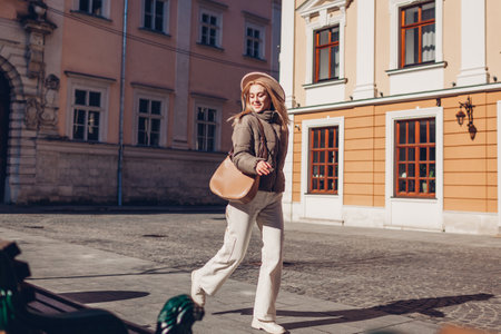 Full body portrait of stylish young woman walking on city street wearing stylish hat and brown jacket. Spring fashionの写真素材