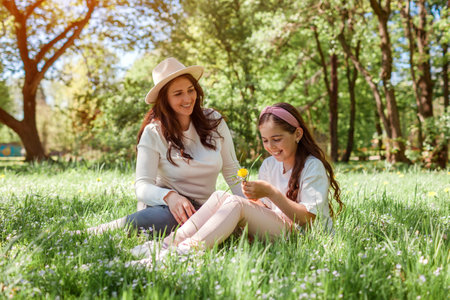 Mother's day. Mother and her daughter relaxing on grass in spring park. Family having fun outdoors picking flowers spending time togetherの写真素材