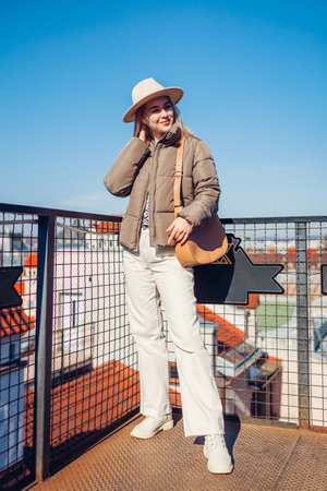 Full body portrait of stylish young woman enjoying city view wearing stylish hat outdoors. Spring fashion. Beige white and brown clothes and accessories.の写真素材