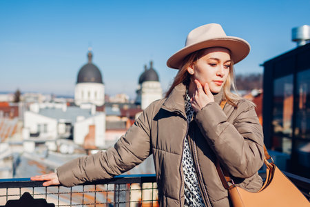 Portrait of young woman enjoying warm weather and city roof tops landscape. Spring outdoor fashion. Girl wears beige hatの写真素材
