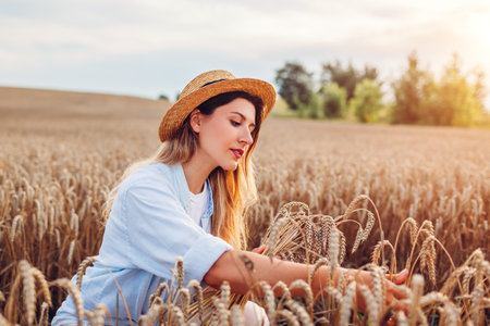 Portrait of young woman picking wheat in summer field wearing straw hat at sunset. Young farmer checking harvestの写真素材