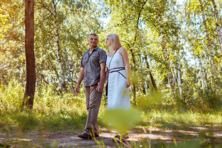 Senior family couple walking outdoors in summer forest. Elderly people holding hands. Romantic date. Man and woman enjoy landscapeの写真素材