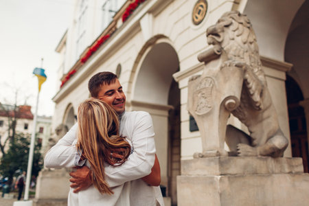Happy couple in love walking in old Lviv city wearing traditional ukrainian shirts. Young people hug by town hall lionの写真素材