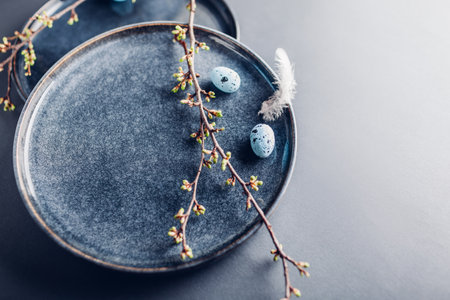 Easter dish decorated with blue eggs, feathers and spring branches. Ceramic plate on grey background. Space. Holiday mockupの写真素材